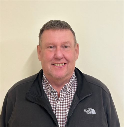 Photograph of a man with short hair wearing a chequered shirt and outdoor fleece. He has a friendly expression and stands against a plain, light-coloured background. Photograph of a man with short hair wearing a chequered shirt and outdoor fleece. He has a friendly expression and stands against a plain, light-coloured background.